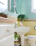 A bathroom with mint green-colored walls and yellow tiles has a toilet, windows, and a sink