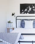 Black metal bed with striped pillows, monochrome floral art, and bedside tables with plants and lamps.