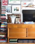 Mid-century modern dresser with a TV, books, framed art, and a tall plant in a bright living room.
