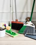 Cleaning supplies including a broom, dustpan, mop, and a caddy with brushes and spray bottle on a wooden floor.