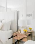 White bedroom with mirrored walls, plush pillows, gold-accented side tables, and yellow flowers in vases.