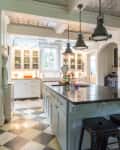 Spacious kitchen with checkered floor, large island, black stools, pendant lights, and glass cabinets.