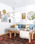Cozy living room with a gray sectional, wooden coffee table, patterned rug, wall art, and a large potted plant.