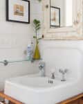 Bathroom with vintage sink, distressed mirror, framed art, green vase, and candles on a white shiplap wall.