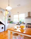 Bright kitchen with wooden floors, white cabinets, fruit bowl on island, and staircase leading to upper level.