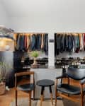 Walk-in closet with hanging clothes, shoe racks, two chairs, plants, and shelves with folded towels and baskets.