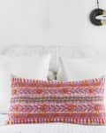 Bed with white pillows and a colorful embroidered cushion, blue lamp, and wall art in a bright bedroom.