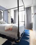 Modern bedroom with a four-poster bed, geometric wallpaper, checkered curtains, and blue rug.