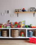 Children's playroom with toys on a white shelf, wicker baskets, and a red toy wagon on the floor.