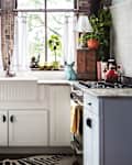 Bright kitchen with white cabinets, a farmhouse sink, and a gas stove. Decorated with plants, a blue rabbit figurine, and a red kettle.