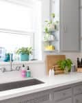 Gray kitchen with white countertops, potted plants, cutting board, knife set, and a bowl of red apples.