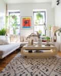 Living room with a beige sectional sofa, plants, abstract art, and a patterned rug on wooden floor.