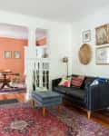 Living room with black leather sofa, colorful cushions, red patterned rug, and adjacent dining area with wooden chairs.