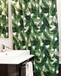 Bathroom with green leaf-patterned shower curtain, white sink, stacked towels, and wooden storage shelves.