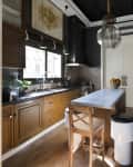 Narrow kitchen with wooden cabinets, island with barstool, pendant light, and fruit bowl on counter.