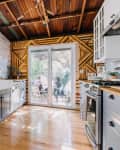Rustic kitchen with gray cabinets, wooden countertops, brick accents, and sliding glass doors leading to a patio with people.