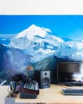 Desk setup with computer monitor, keyboard, speakers, and audio mixer, against a large mountain landscape poster.
