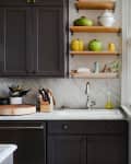 Dark kitchen cabinets, marble countertop, open shelves with colorful pots, and a patterned yellow and white wall.