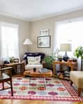 Cozy living room with patterned rug, plants, wooden furniture, and framed photos on beige walls.