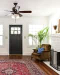 Living room with black door, red patterned rug, brown armchair, blue ottoman, and white brick fireplace.