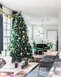 Living room with a decorated Christmas tree, gray sectional sofa, and dining area with green chairs in the background.