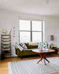 Living room with green sofa, patterned cushions, round wooden coffee table, and tan armchair on a gray patterned rug.