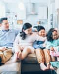 Family of five laughing together on a beige sofa in a bright, modern living room.