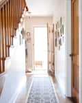 A door opens and leads to an elongated hallway where a runner or area rug can be seen