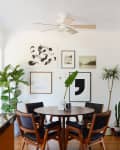 Dining area with round wooden table, black chairs, potted plants, and framed art on white walls.