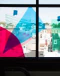 Colorful transparent sheets taped to a window overlooking a cityscape.