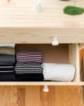 Open wooden drawer with neatly folded clothes in various colors and patterns on a hardwood floor.
