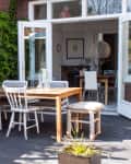 Patio with wooden table, white chairs, and green ivy wall, leading to an open dining room with modern decor.