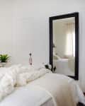 Cozy bedroom with white bedding, fluffy pillows, a large mirror, and a black-and-white landscape photo above the bed.