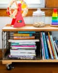 Wooden shelf with books, a toy ferris wheel, colorful stacking rings, a jar, and a crate of blocks.