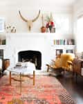 Eclectic living room with a white sofa, colorful rug, fireplace, and mounted bull skull, featuring bookshelves and a TV console.