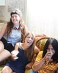 A group of three girlfriends laughing on the couch with cocktails