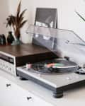 Turntable with vinyl record, stereo receiver, and potted plants on a white cabinet.