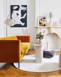 Mid-century modern living room with mustard sofa, pink swivel chair, abstract art, and round dining table.