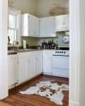 Cozy kitchen with white cabinets, a gas stove, a cowhide rug, and a wall clock above the counter.