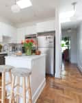 White kitchen with brick accent wall, island with stools, stainless steel appliances, and tulips in a vase.