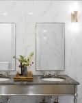 Double vanity with marble countertop, two mirrors, floral arrangement, and wall sconces in a tiled bathroom.