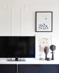 A television and TV stand in front of a white wall adorned with artwork and intricate molding