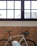 Loft space with large windows, exposed brick wall, potted snake plant, and a white bicycle.
