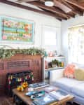 Cozy living room with white sofa, colorful pillows, brick fireplace, and vibrant artwork above mantel.