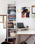 Home office with a white desk, laptop, bookshelves, wall art, and decor items like a lamp and plants.