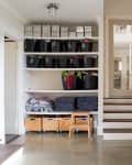 Organized entryway with shelves of black baskets, labeled boxes, folded blankets, and a small wooden step stool.