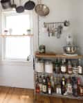 Small kitchen with hanging pots, spice rack, white stove, mixer, and shelves with bottles and jars.