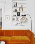 Orange velvet sofa in front of a white built-in bookshelf with art, plants, and a shell floor lamp.