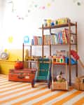 Colorful children's playroom with books, toys, a striped rug, and a wooden shelf.