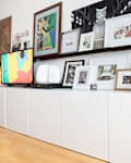 Modern living room with white cabinets, colorful abstract TV display, framed art, and decor on shelves.
